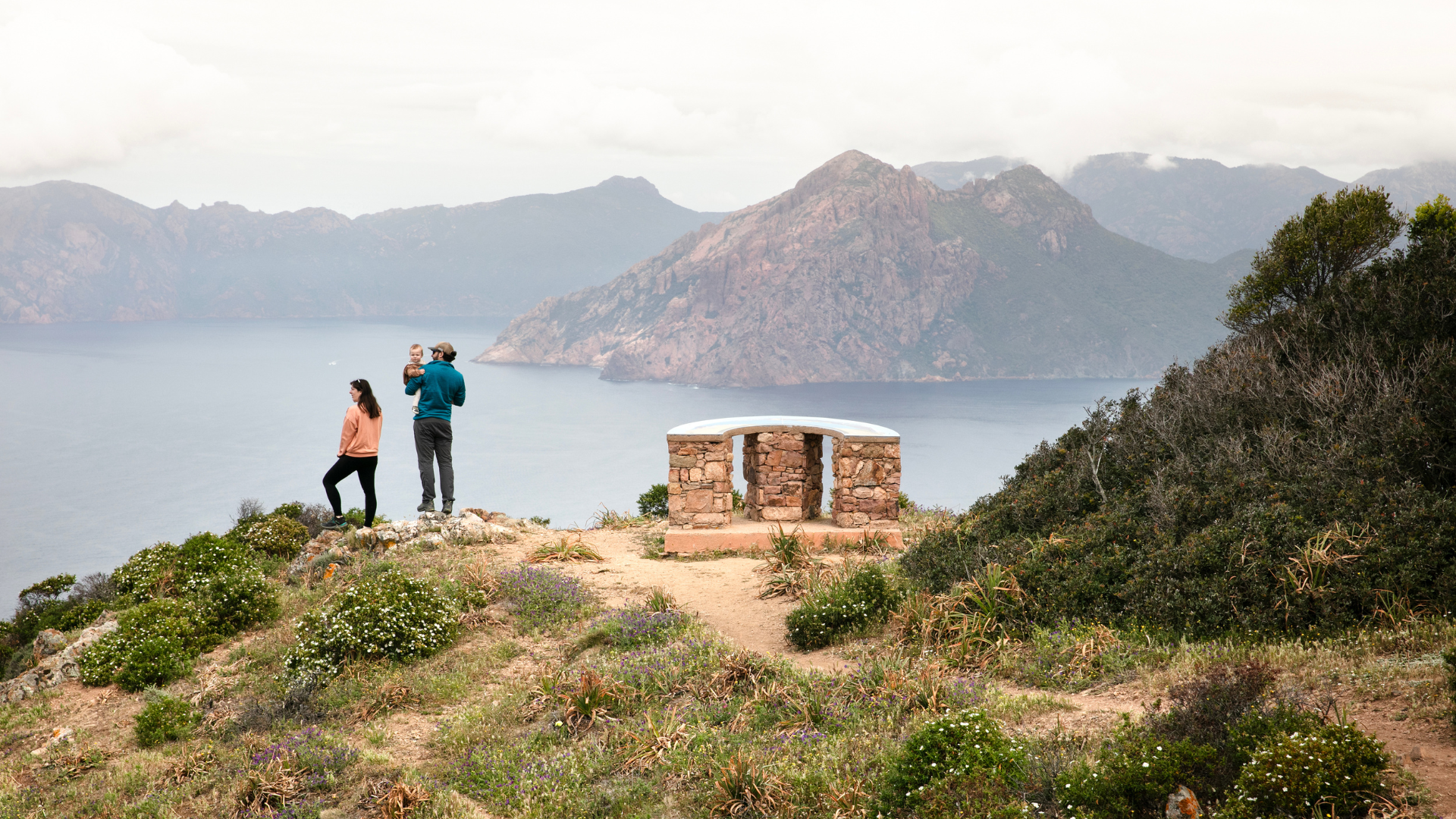 Famille avec bébé contemple le paysage face à la mer en Corse